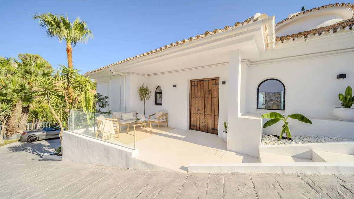 Entrance of Villa Zentosa with a wooden double door, white walls and a shaded porch